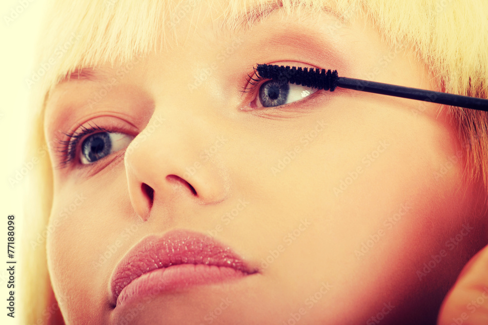 Young woman doing make up on eyelashes.