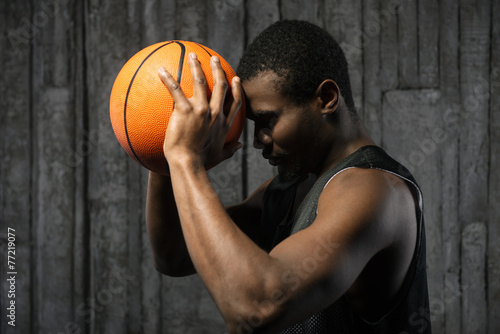Afro-american basketball player pressing ball to his forehead