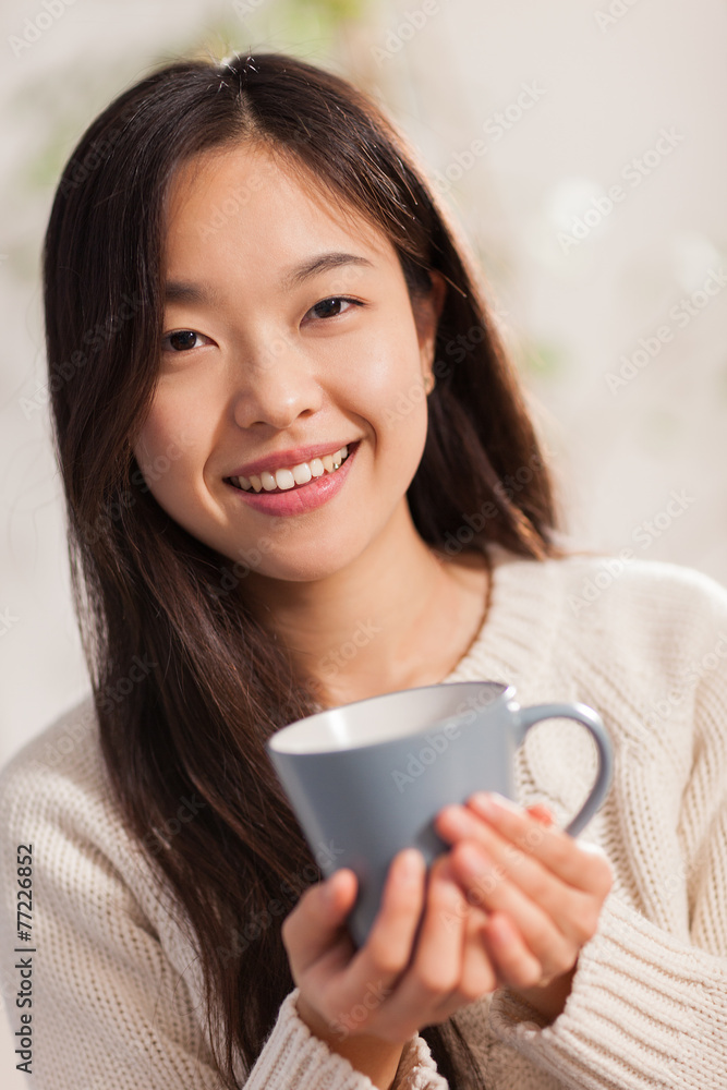 Asian woman with hot mug in her hands smiling towards the camera Asian woman with hot mug in her hands smiling towards the camera