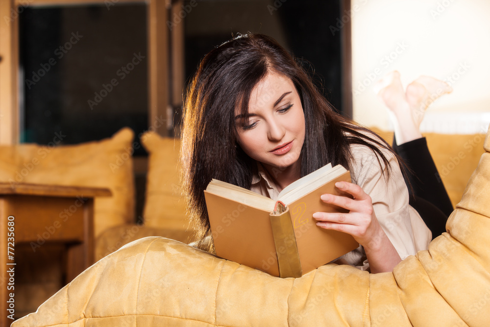 Woman lying on her couch reading a book at home Woman lying on her couch reading a book at home