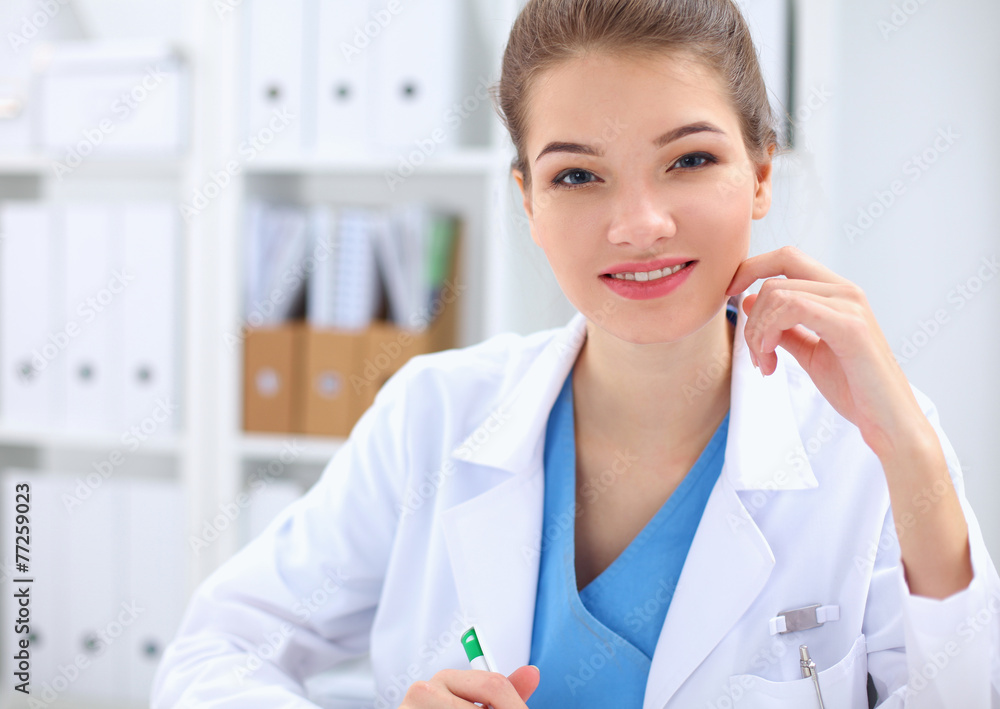 Beautiful young smiling female doctor sitting at the desk . Beautiful young smiling female doctor sitting at the desk .
