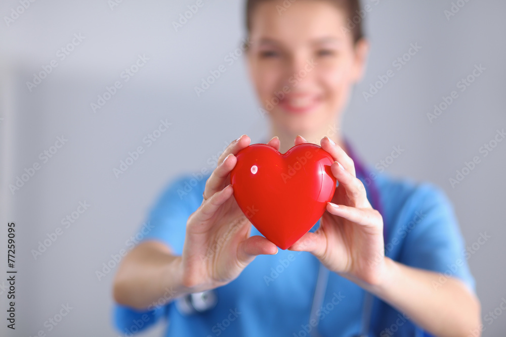 Young woman doctor holding a red heart, standing on gray Young woman doctor holding a red heart, standing on gray