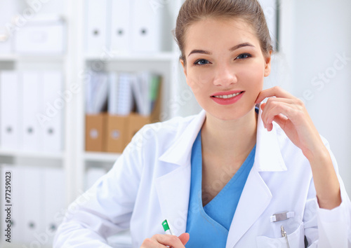 Beautiful young smiling female doctor sitting at the desk .