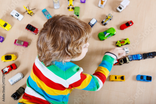 Little blond child playing with lots of toy cars indoor