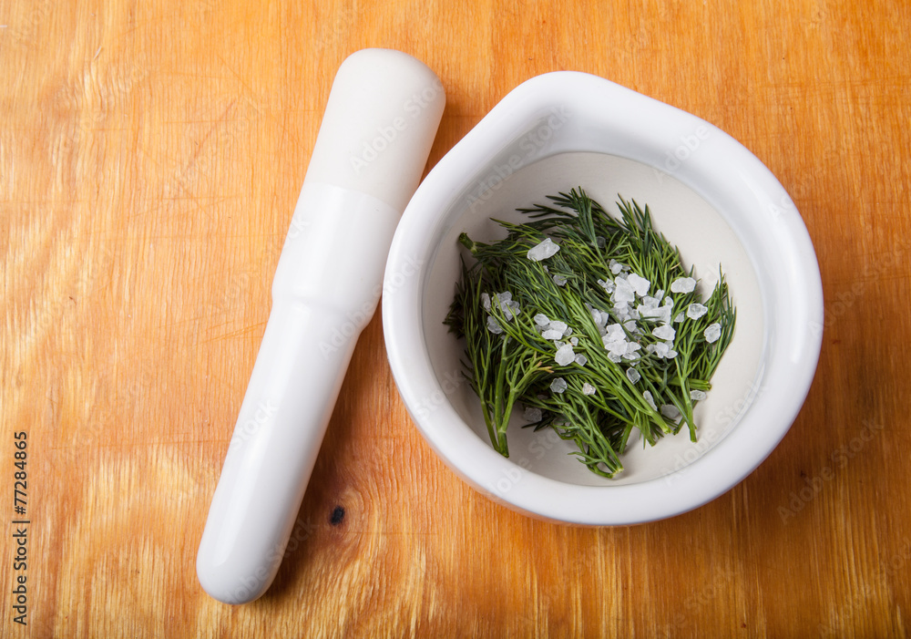 mortar with pestle and dill and salt on a wooden table.
