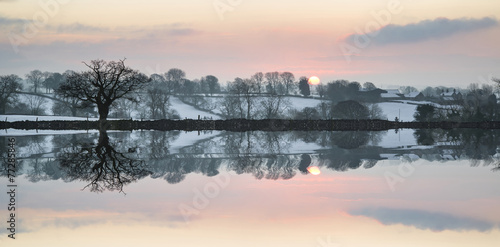 Snow covered Winter countryside sunrise landscape reflected in s