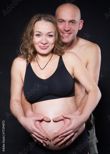 a pregnant woman with her husband hugging her from behind