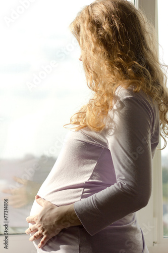 Beautiful pregnant blonde standing near the window