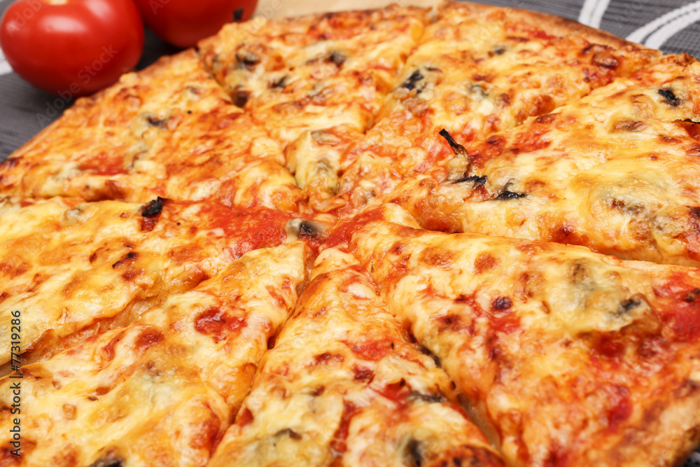 Pizza, geschnitten mit Tomaten im Hintergrund