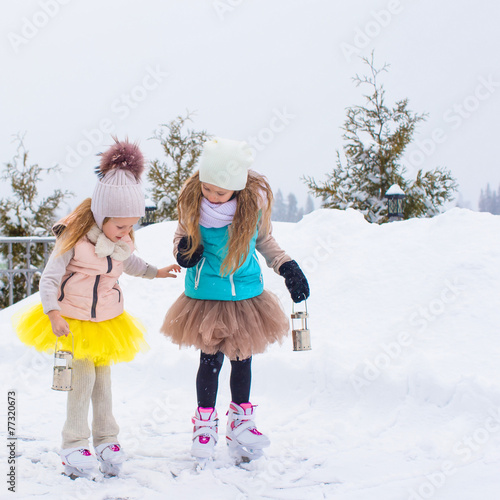 Adorable little girls skating on ice rink outdoors