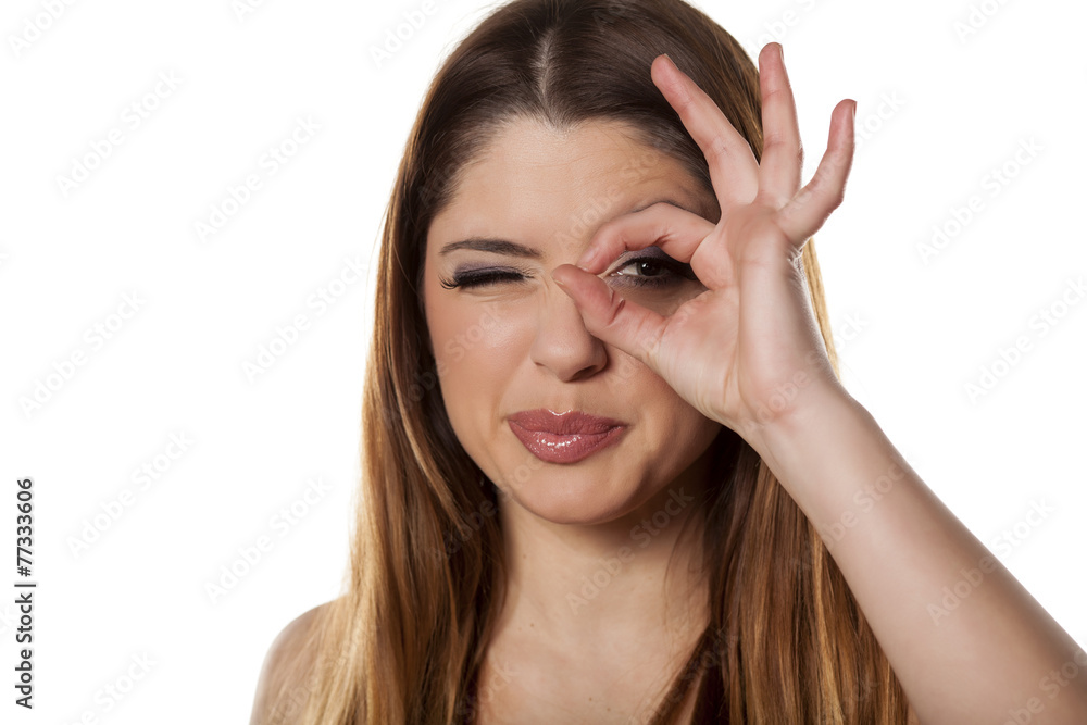 young woman peeking through a hole of her fingers young woman peeking through a hole of her fingers