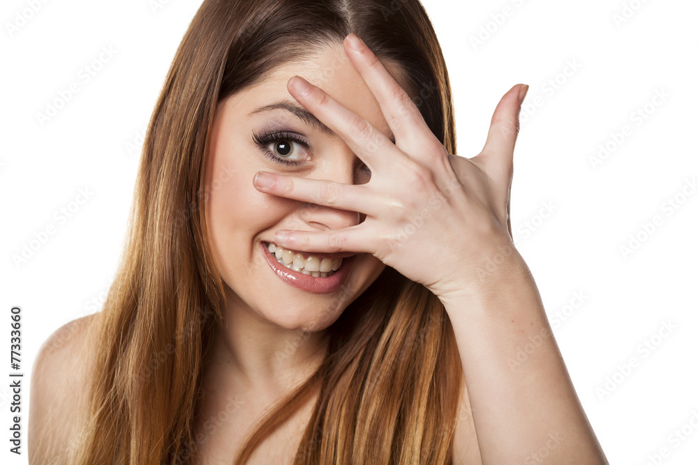 Smiling young woman peeking through her fingers Smiling young woman peeking through her fingers