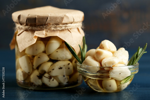 Canned garlic in glass jar on color wooden background