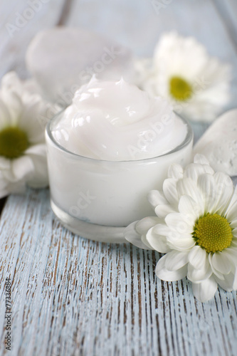 Cosmetic cream with flowers and spa stones on wooden background