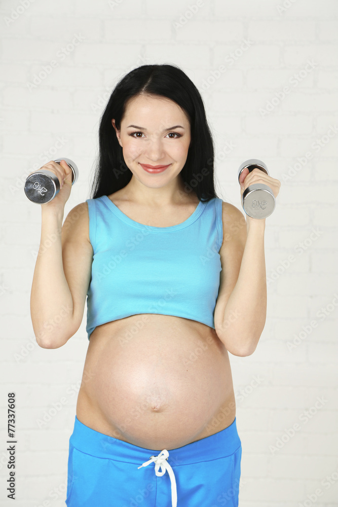 Young pregnant woman with dumbbells on light background Young pregnant woman with dumbbells on light background