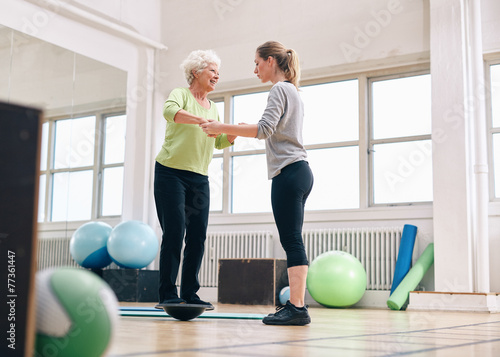 Valokuvatapetti Trainer helping senior woman on bosu balance training platform