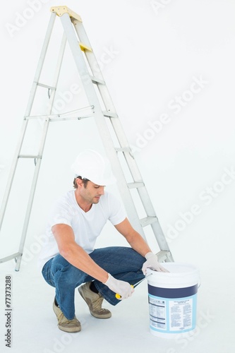 Man crouching while opening paint pot