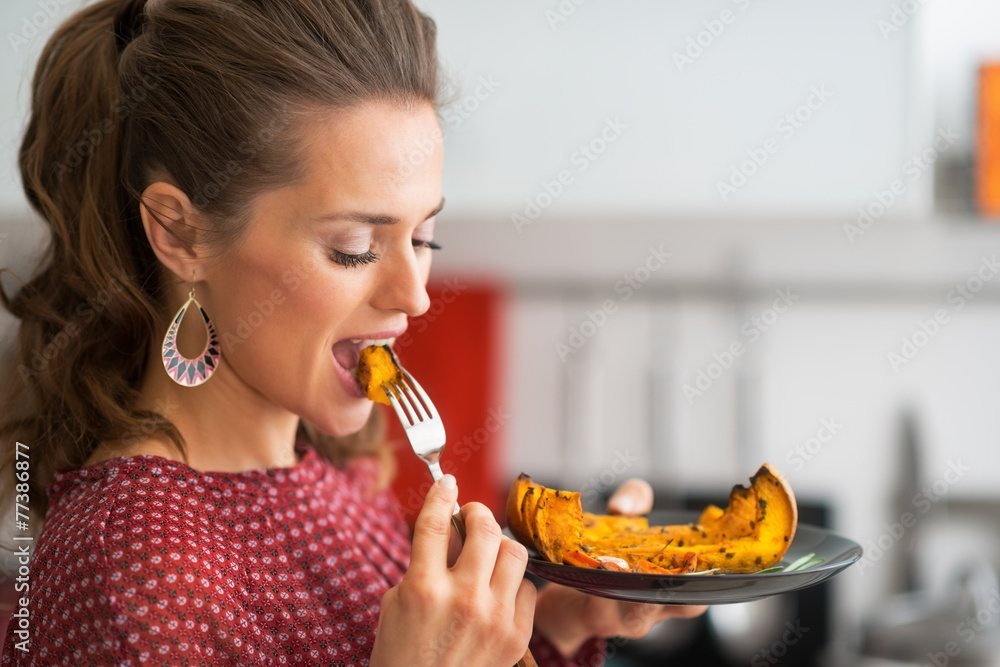 Portrait of young woman eating baked pumpkin in kitchen Portrait of young woman eating baked pumpkin in kitchen