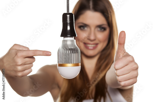 Young smiling woman pointing on LED bulb, and showing thumb up photo