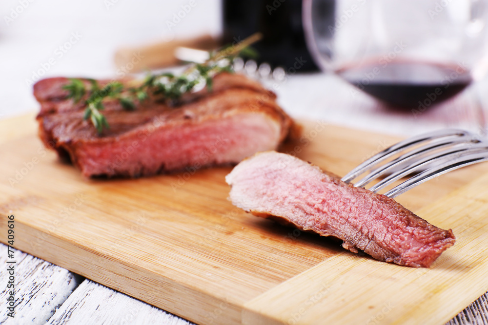 Steak with herbs on wooden stand and wine on table close up