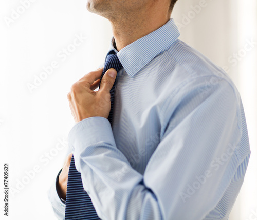 close up of man in shirt adjusting tie on neck