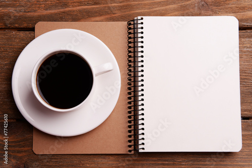 Cup of coffee on saucer with notebook on wooden table