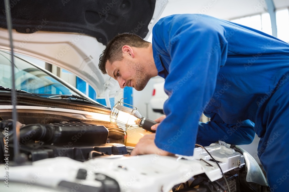 Mechanic examining under hood of car with torch Mechanic examining under hood of car with torch