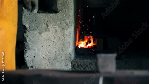 Blacksmith is blowing up air in the furnace to get sparkles and starts shaping the metal photo