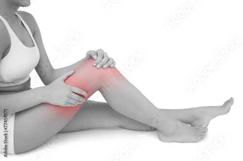 Slim woman sitting on floor touching her injured knee