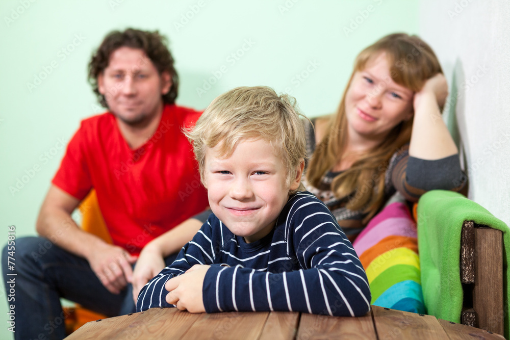 Young smiling blond hair son sits on foreground of his parent