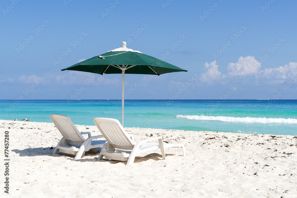 Pair of sun loungers and umbrella on a tropical beach in Cancun,