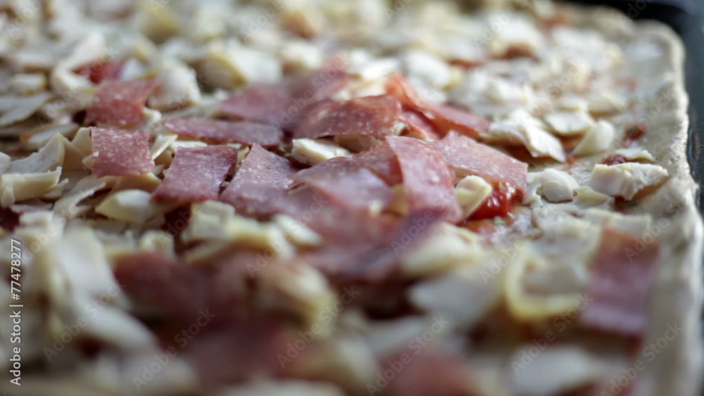 Close up shot of a black baking sheet with dough and a person who is putting on different kinds of ingredients for pizza Close up shot of a black baking sheet with dough and a person who is putting on different kinds of ingredients for pizza