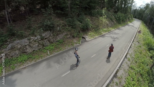 AERIAL: Skaters on longboard driving in slow motion through forest photo