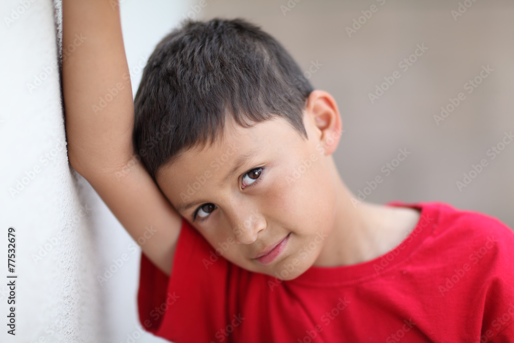 Serious young boy leans against wall Serious young boy leans against wall