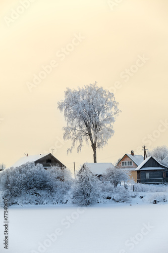 Frozen lake shore with timber houses covered with snow, sunset
