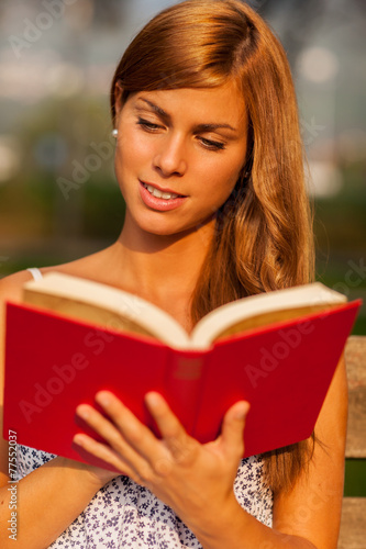 brunette woman is reading a book on a bench