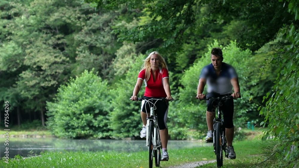 HD1080p: Young couple cycling in nature near the lake towards camera HD1080p: Young couple cycling in nature near the lake towards camera