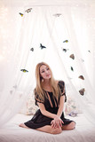 Beautiful young woman sitting on the white bed with butterfly. 