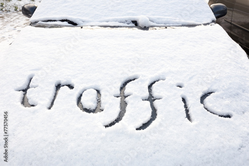 Word traffic written in snow on engine hood of car