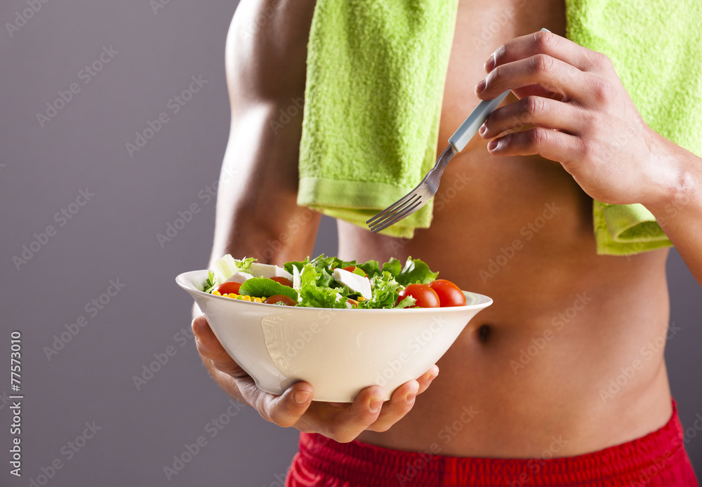 Fit man holding a bowl of fresh salad on grey background Fit man holding a bowl of fresh salad on grey background