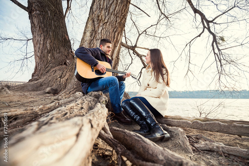 Young couple sitting on the tree, playing guitar and singing