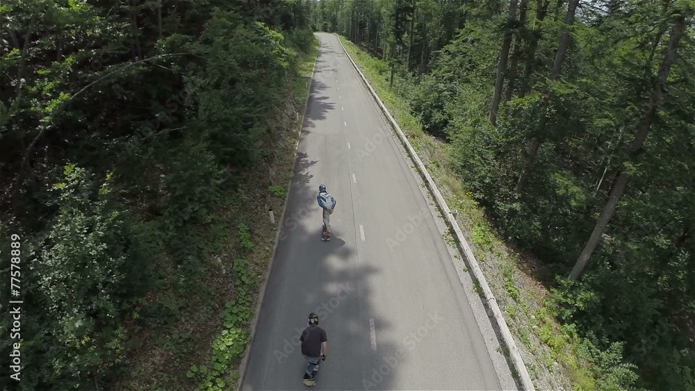Flying over two longboarders speeding down the road in woods Flying over two longboarders speeding down the road in woods