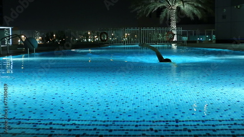 attractive blonde women swimming a luxury pool at night