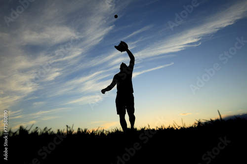 A man silhouetted by the sunset is just beginning catch ball