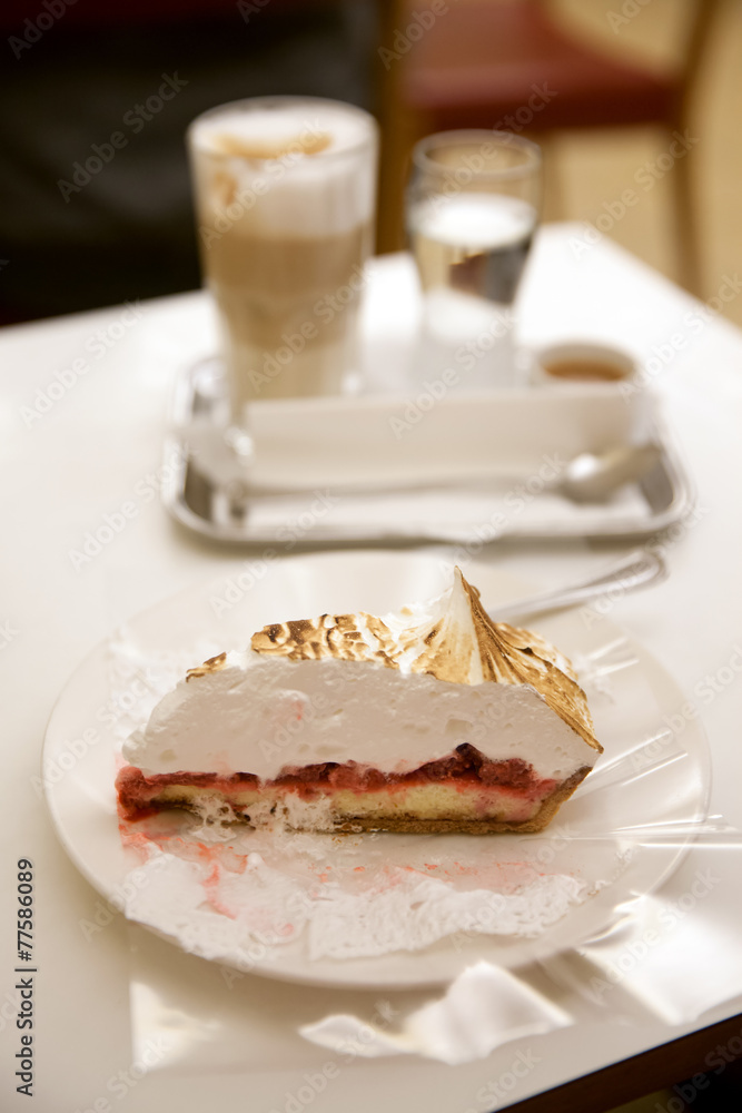 The piece of sweet cake on white table against glass of coffee