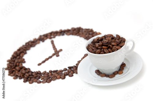 The white cup of coffee bean in front of grain clock