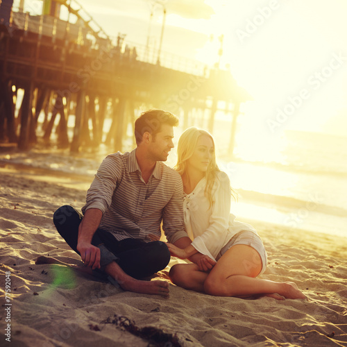 romantic couple sitting on beach with golden sunset by beach