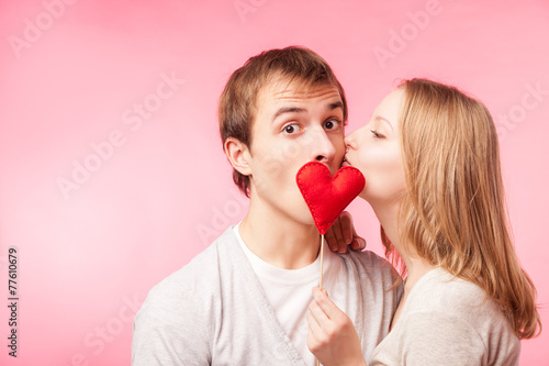 Girl kissing boy hiding behind a little red heart