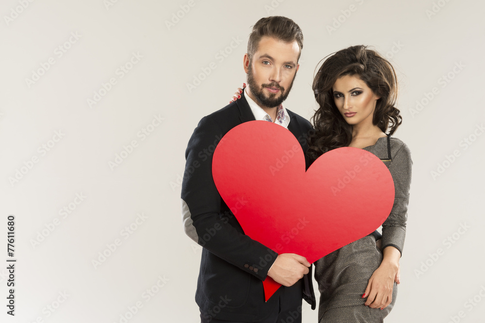 young smiling caucasian couple holding sign in form of red heart