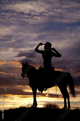 silhouette of a woman sitting on a saddle hands on hat